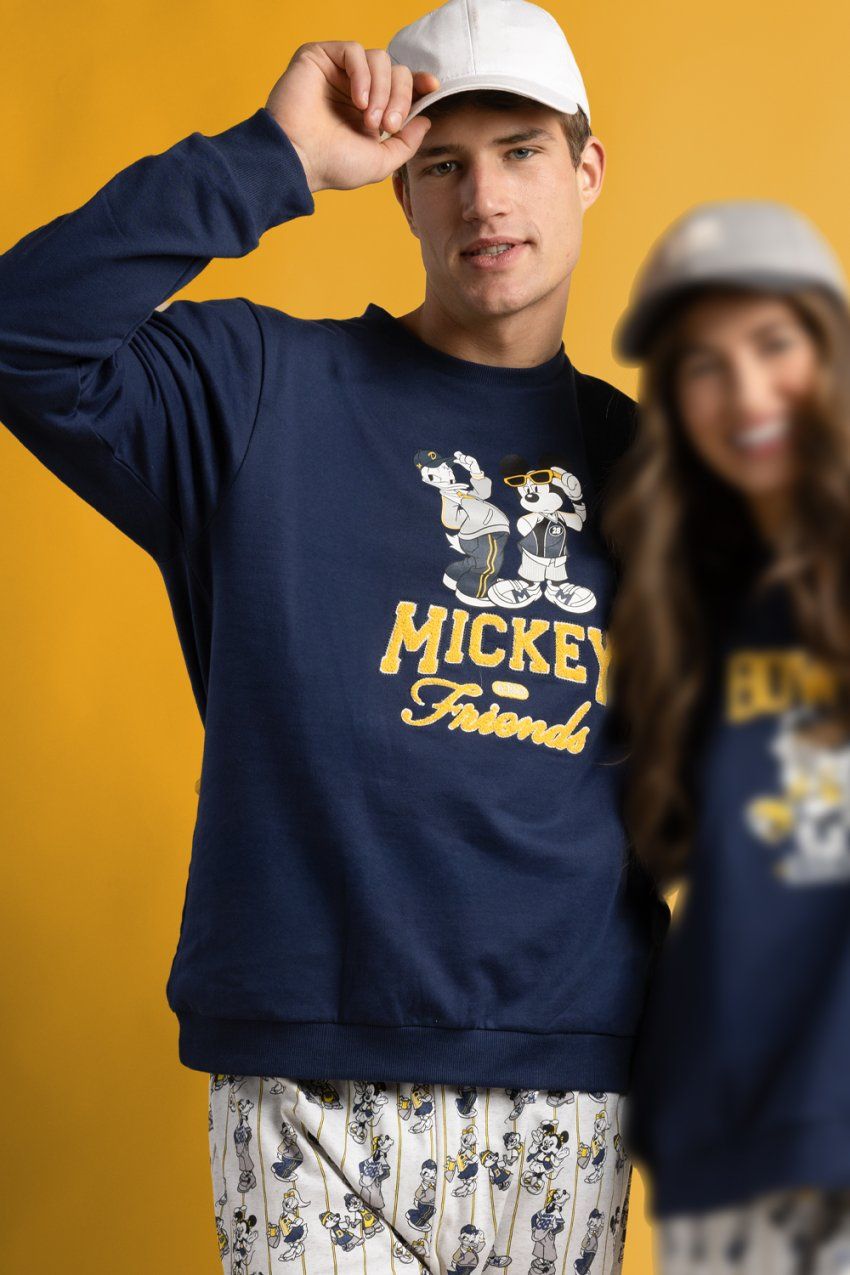Modelo con pijama de hombre Disney Varsity Squad 64919, con sudadera azul marino con dibujo Disney y letras en contraste, y pantalón largo estampado.