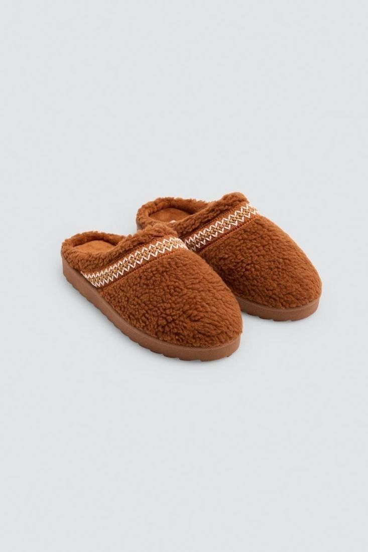 Zapatillas de casa para mujer Ysabel Mora 14181 en color camel, con acabado de borreguito, tira decorativa a contraste y diseño destalonado.