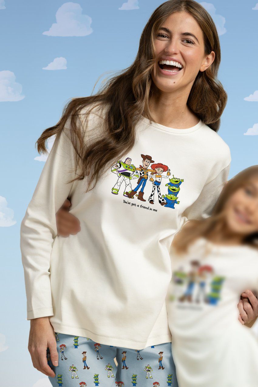Modelo con pijama de mujer Disney Toy Story 64677, con camiseta de manga larga color crudo con dibujo de los personajes y pantalón azul claro estampado.
