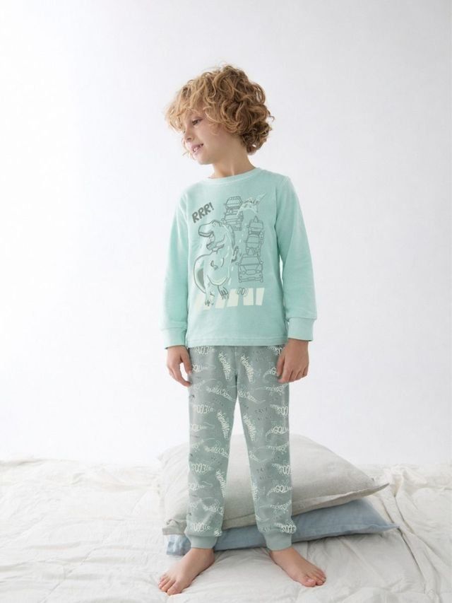 Pijama de niño Katuco con camiseta verde agua estampada de dinosaurio y vehículos, y pantalón verde grisáceo con motivos de dinosaurios.