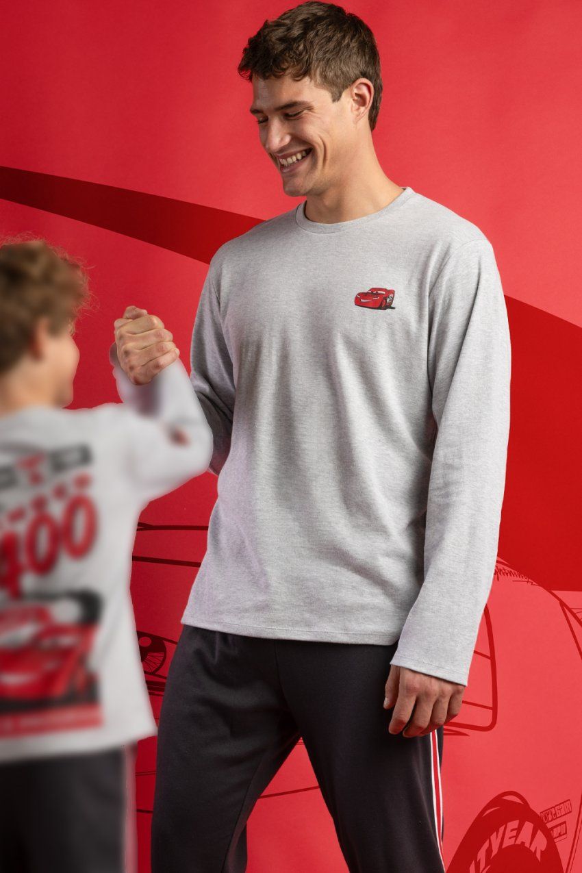 Modelo con pijama de hombre Disney Cars Piston Cup 64915, con camiseta gris jaspeada de manga larga con detalle de Cars en el pecho y pantalón largo oscuro.
