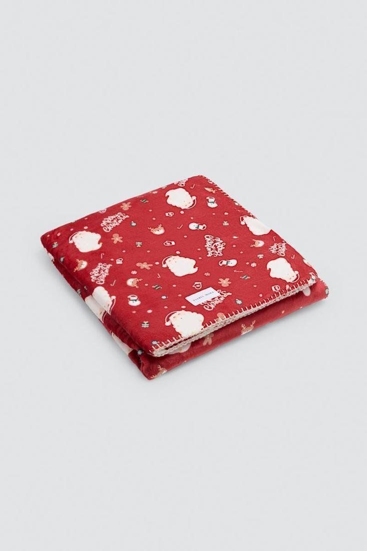 Manta roja doblada con estampado de Papá Noel, copos de nieve y pequeños motivos navideños.