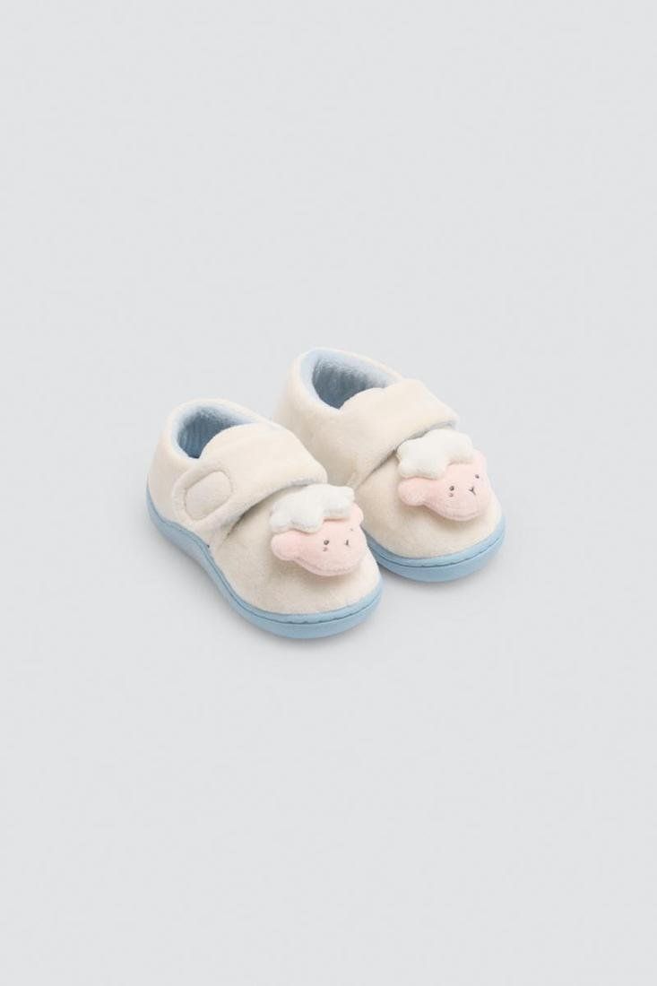 Vista lateral de zapatilla infantil Ysabel Mora 54046 en crudo, con detalle de ovejita en relieve, cierre de velcro y suela azul claro.