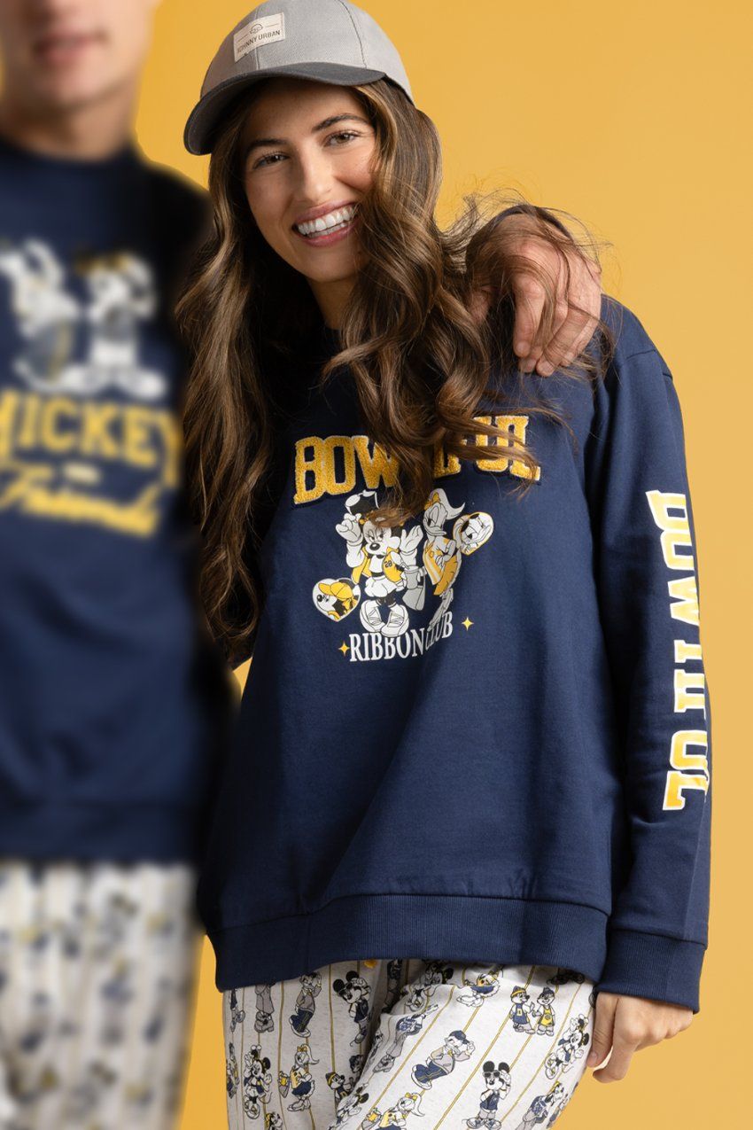 Modelo con pijama de mujer Disney Varsity Squad 64675, con sudadera azul marino con dibujo Disney y letras en contraste, y pantalón largo estampado.